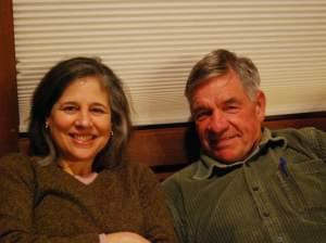 A middle-aged couple sitting together on a couch, smiling.