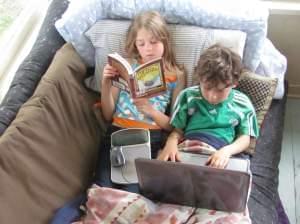 one child reads while another looks at a computer screen