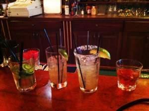 Several cocktails lined up on a bar.