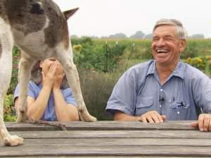 A dog jumps onto a picnic table. A man and a woman are sitting at the table and are laughing.