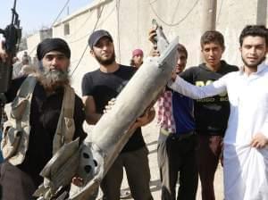 Islamic State militant stands next to Raggah residents on September 16th, holding wreckage of a Syrian war plane.