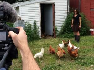 A woman stands outside with several chickens as she's having her photo taken.