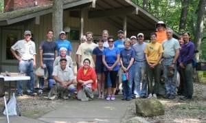 A wide shot of 20 people in two rows outdoors in front of a low building.