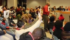 Community activist Martel Miller of Urbana holds up a flyer of Champaign Police Officer Matt Rush, along with several other protesters, at Tuesday's Champaign City Council meeting.