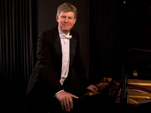 Ian Hobson standing next to a piano