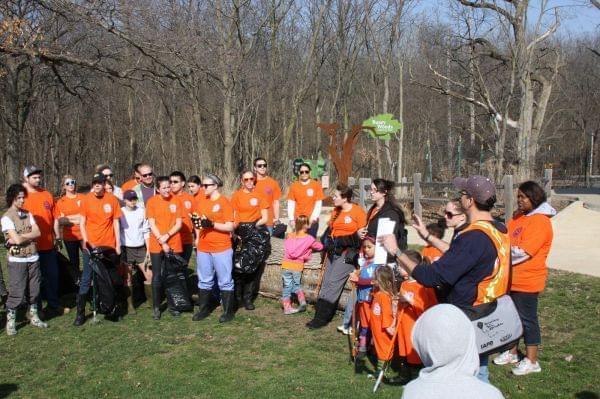 A sunny, outdoor shot of a crowd in matching orange t-shirts listening to organizers.