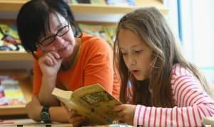 Young girl reading a book with an older woman.