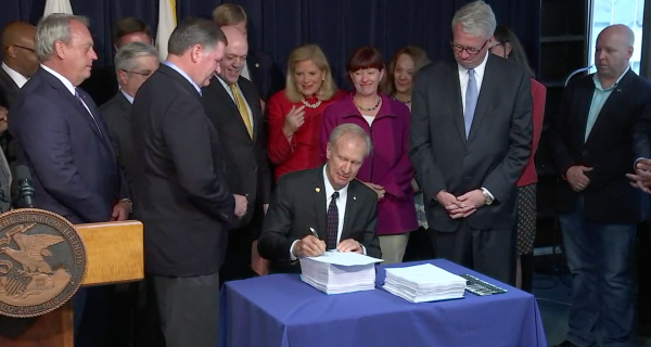 Gov. Bruce Rauner signs the FY2019 budget, surrounded by the Democratic and Republican legislators who negotiated it, at the James R. Thompson Center in Chicago.