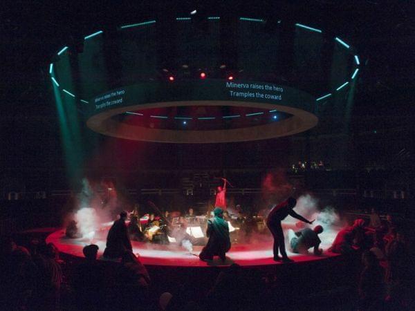 people perform on a round stage with orchestra in the middle