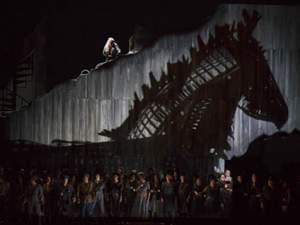 Woman sits atop a stage overlooking crowd and a metal trojan horse