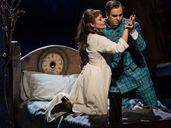 A man and woman embrace on a bed on a stage