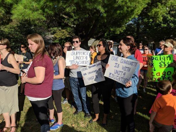 Union members stand in the grass outside the Unit 4 administration building carrying signs.