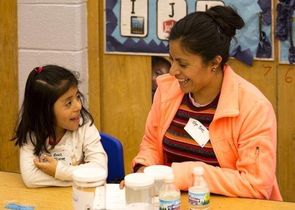 A woman and child are sitting at a table together.  They are smiling at each other.