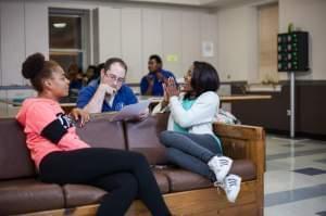 An employee at the Night Ministry talks with two residents of the program while they sit on a couch in a meeting room.