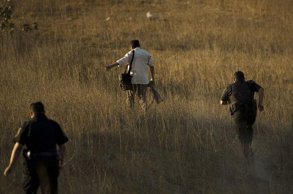 Police officers run after a photographer trying to reach a better view of a crime scene where a police officer was killed in Rosarito, Mexico, Thursday, Oct. 23, 2008.