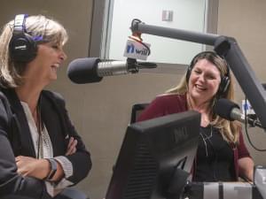 two women sit in a radio studio talking in front of microphones 