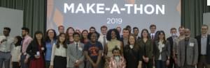 Winners of the first Health Make-A-Thon hosted by the Carle Illinois College of Medicine at the University of Illinois pose with U of I staff. Standing in a row in front a  projector screen. 