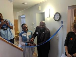 Two people holding scissors about to cut a blue ribbon