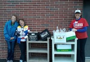 lunch ladies standing with boxes of bagged lunches and breakfasts behind a brick school building