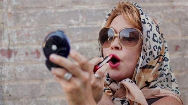 woman looking in a mirror putting on lipstick and wearing a scarf on her head