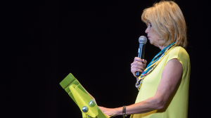 Women in yellow outfit stands on stage with a microphone