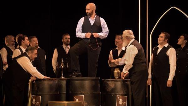 Man stands on barrel surrounded by other men looking up at him