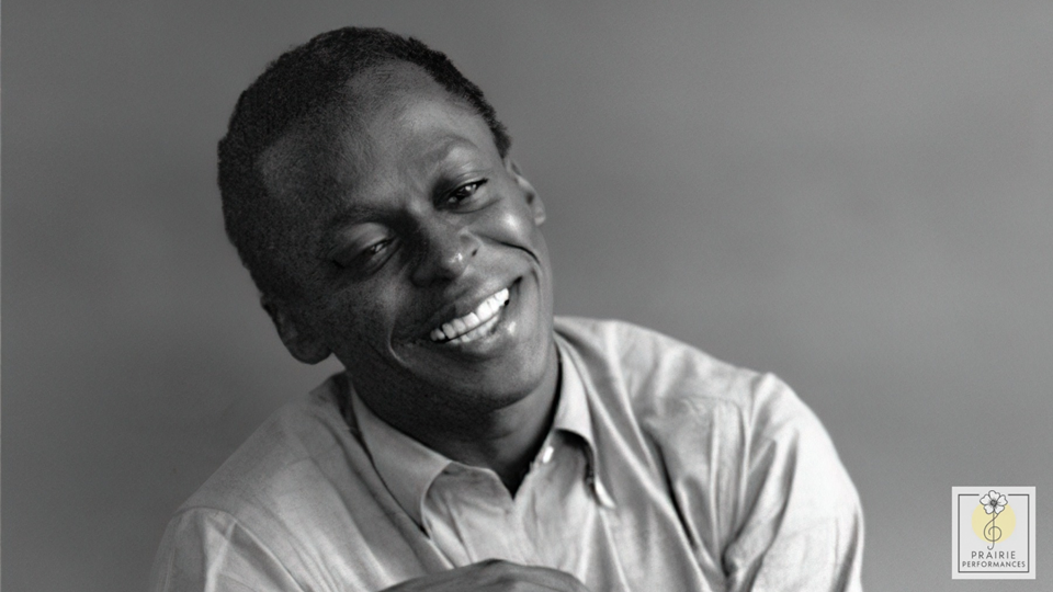 Miles Davis smiles, looking relaxed with his head tilted to the side.