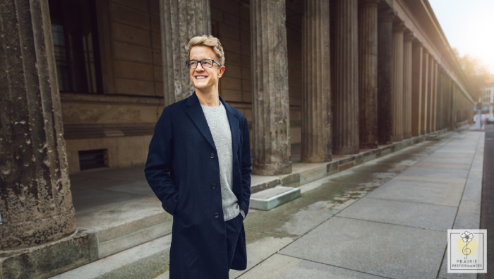 A blonde man in glasses standing on a street. 