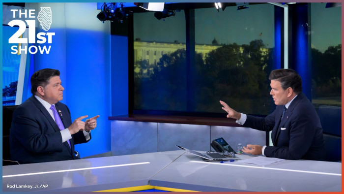 Pritzker, on a mostly blue TV news set, points his index fingers toward host Brett Baier, who raises his right hand as though he's about to palm a basketball; both men are wearing navy blue suits, Pritzker is spoting a purple necktie while Baier's is dark blue.
