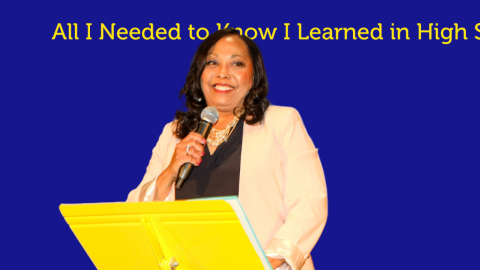 woman standing on stage behind a yellow stand holding a microphone