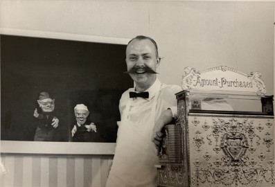 Man stands at candy counter with puppets behind him