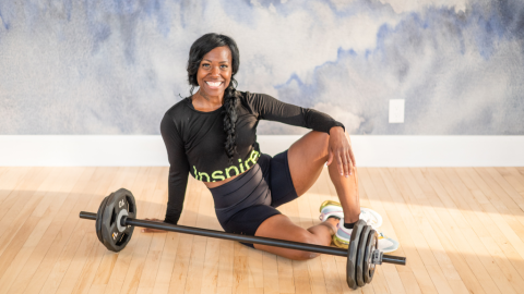 Woman sits on floor behind barbell