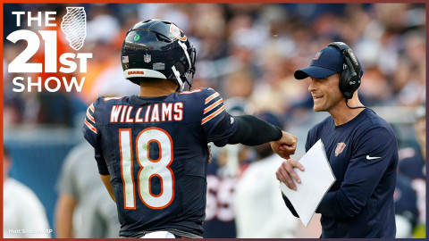 Williams, wearing his helmet and the Bears' navy blue home jersey, extends his arm toward coach Ben Johnson as though seeking a fist bump; Johnson wears a long-sleeve navy shirt with the bear head logo on the left chest and a Bears baseball cap; he's also wearing a radio headset and holding a laminated document