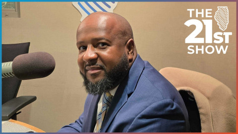 Sean Brown wearing a dark blue suit and necktie, sitting in front of an Electrovoice RE-20 microphone in the beige studios of Illinois Public Media