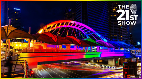 a long-exposure image of a bridge lit up in the rainbow colors of the pride flag as the lights of vehicles streak underneath