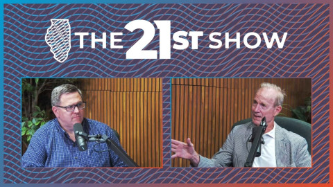 two white men are pictured in a wood-paneled podcast studio; one is wearing a purple button-down shirt; the other is wearing a white polo shirt under a seersucker jacket