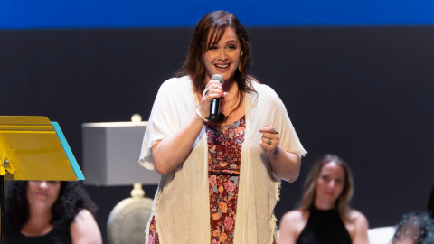 woman smiles while holding microphone and standing on stage