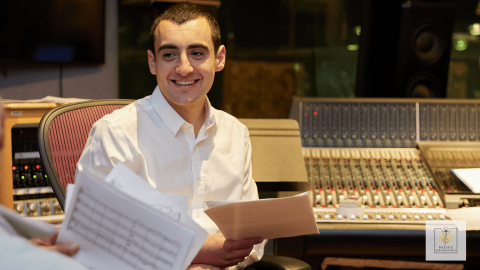 A man sitting at a recording console holding paper music sheets.