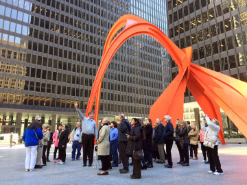 A tour group gathered under an outdoor sculpture in Chicago